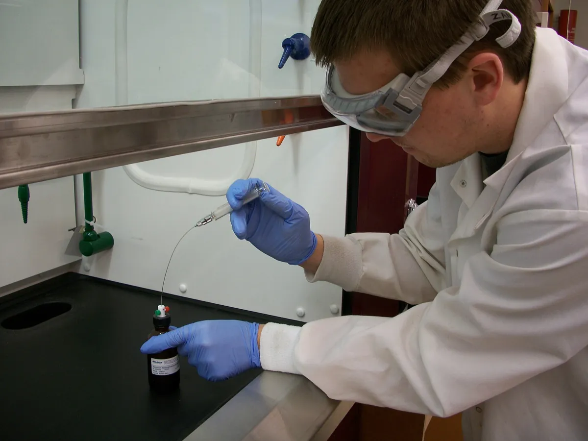A chemist drawing liquid into a syringe inside a fume cupboard