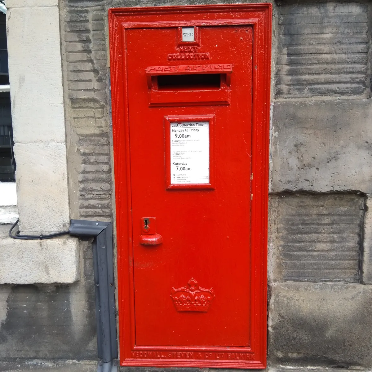 A red Royal Mail wall post box set into a stone wall